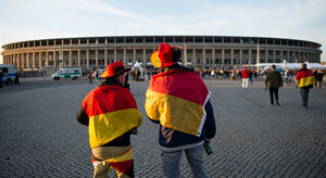 Zwei Männer, gehüllt in Deutschland-Fahnen, vor einem Stadion