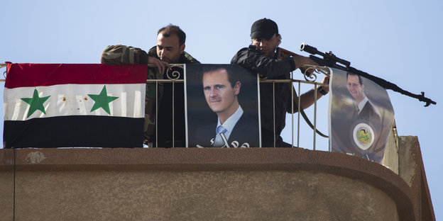 Soldaten mit Gewehr hinter einem Zaun, an den ein Porträt des syrischen Machthabers Assad gehängt ist