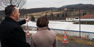 Mann und Frau von hinten vor einem Zaun, dahinter Zelte und Hügel