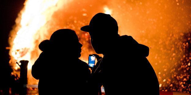 zwei Menschen vor Feuer mit Smartphone in den Händen