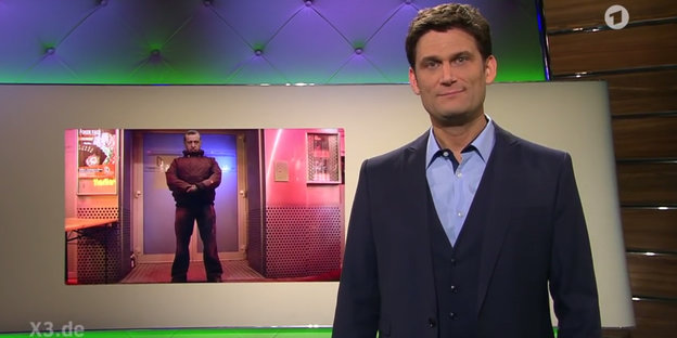 Mann in Anzug, es ist NDR-Moderator Christian Ehring, vor einem Schaubild mit einem Mann drauf