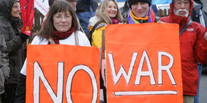 TeilnehmerInnen eines Ostermarsches halten Schilder mit der Aufschrift „No War“ in den Händen