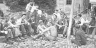 Ein Schwarz-Weiß-Foto, darauf Männer, die inmitten von Schutt sitzen und Pause machen