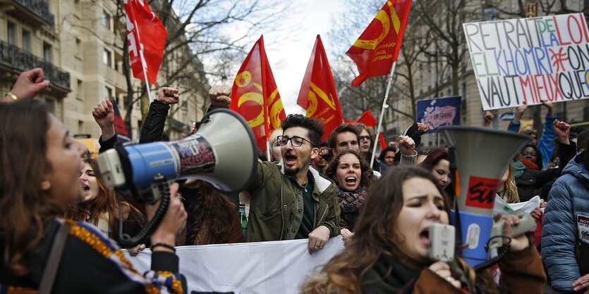 Junge Menschen rufen in Megaphone, recken ihre Hände in die Luft und schwenken Banner und Fahnen