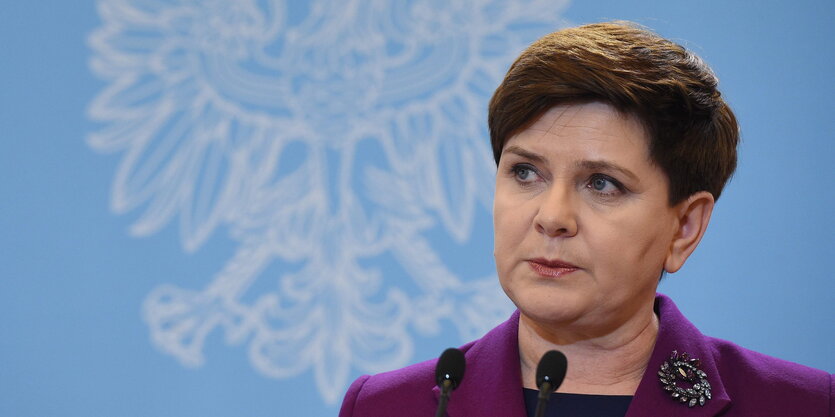 Eine Frau, es ist Beata Szydlo, steht vor einer blauen Wand