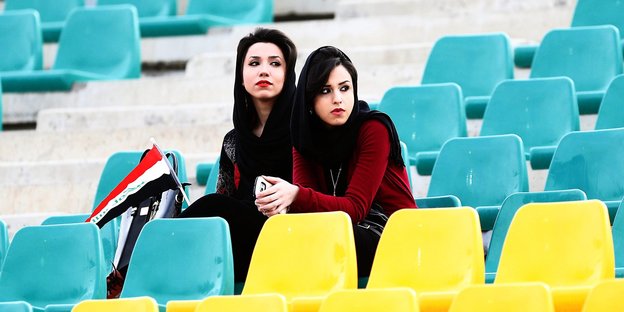 Zwei junge Frauen sitzen auf der Zuschauertribüne eines Sportstadions.
