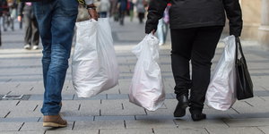 Zwei Menschen, aufgenommen von hinten, tragen Einkäufe in Plastiktüten