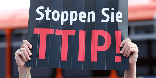 Zwei Hände halten ein schwarzes Schild, auf dem in weißer Schrift "Stoppen Sie" und in schwarzer "TTIP" steht