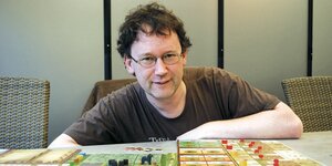 Uwe Rosenberg sitzt vor dem von ihm entwickelten Brettspiel 