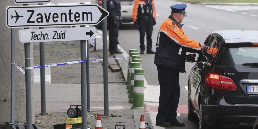 Ein Mann in Uniform steht vor einem Auto neben einem Flughafen-Schild