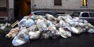 Aufeinandergestapete Mülltüten liegen vor einem Auto auf der Straße