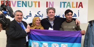 Syrische Flüchtlinge halten eine „Pace“-Fahne, hinter ihnen ein Schild „Benvenuti in Italia“