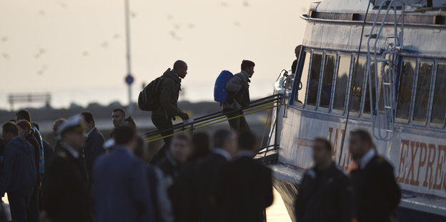 Zwei Flüchtling gehen über einen Steg auf eine Fähre