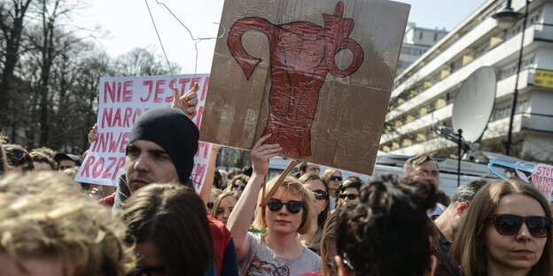 Demonstranten auf der Straße, sie halten Schilder hoch. Auf einem ist ein Uterus zu sehen