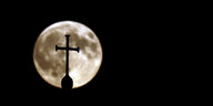 Ein Kreuz vor dem Mond bei Nacht