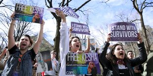 Menschen halten Schilder in die Höhe, auf denen „Free Kesha“ und „I stand with survivors“ steht