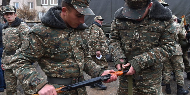 Männer in Militäruniformen, zwei von ihnen halten eine Waffe