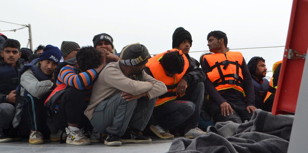 Menschen sitzen in Rettungswesten auf einem Schiff