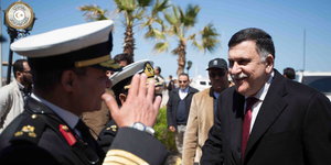 Fajes Serradsch wird von einem salutierenden Militär begrüßt, im Hintergrund Palmen