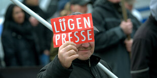 Ein Mann hält eine Stange und einen Zettel mit der Aufschrift „Lügenpresse“