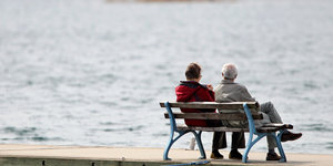 Zwei ältere Menschen sitzen auf einer Bank am See