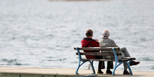 Zwei ältere Menschen sitzen auf einer Bank am See