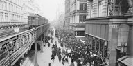 Altes Schwarz-weiß-Foto: Menschen gehen an einer Hochbahn entlang