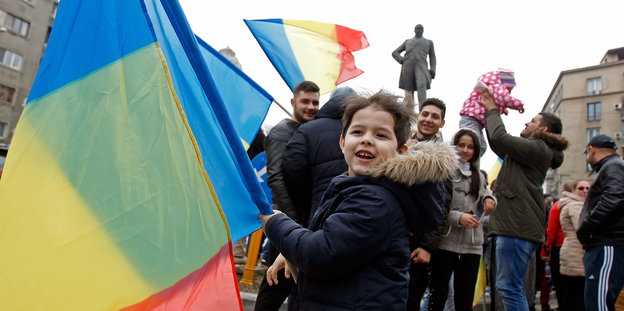 Menschen feiern auf einem Platz in Bukarest, ein kleines Mädchen schwenkt die rumänische Fahne