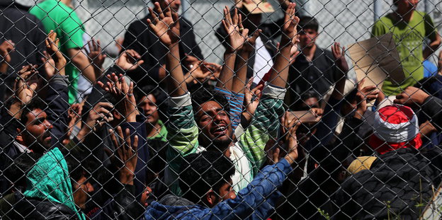 Menschen protestieren hinter einem Zaun