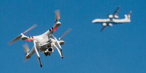 Eine Drohne und im Hintergrund ein Flugzeug vor blauem Himmel