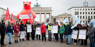 Eine Reihe Menschen hält Schilder, dahinter steht ein großer pinkfarbener Bär