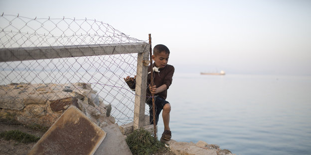 Ein Junge klettert um einen Zaun auf einer Klipp über dem Meer