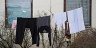 Eine Wäscheleine über der mehrere Kleidungsstücke hängen ist vor zwei Fenstern aufgespannt