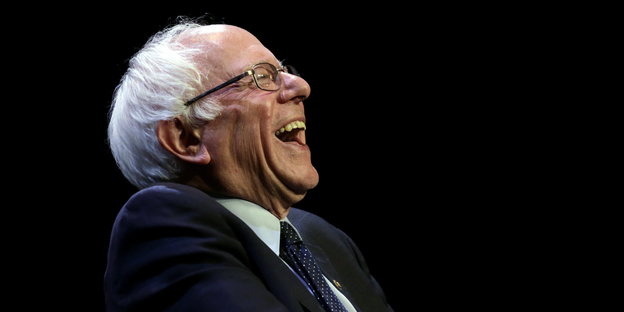 Ein Mann mit weißen Haaren und Brille lacht. Es ist Bernie Sanders