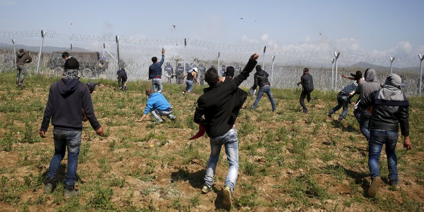 Mehrere Menschen werfen Steine in Richtung des Grenzzauns in Idomeni