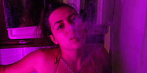 Eine junge Frau in pinkem Licht, Rauch kommt aus ihrem Mund