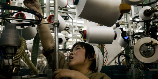 Arbeiterin macht sich an einer Textilherstellungsmaschine zu scahffen - vermutlich in China.