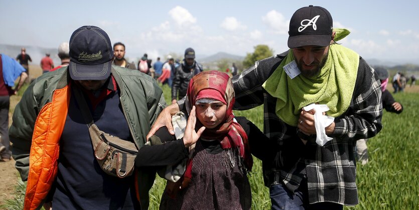 Zwei Männer und eine Frau in der Nähe des Grenzzauns in Idomeni, das Mädchen scheint eine Verletzung vom Tränengas davongetragen zu haben