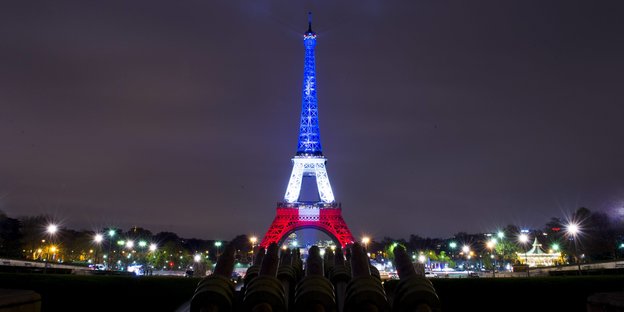 Der Eiffelturm bei Nacht, er wird in den französischen Nationalfarben angestrahlt, Blau, Weiß und Rot