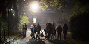 Menschen mit Taschen laufen über eine Straße bei Nacht