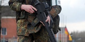 Ein Soldat hält ein Gewehr in der Hand, hinter ihm weht eine Deutschlandfahne