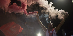 Ein Mann hält ein rotes und ein weißes Rauchsignal in seinen Händen