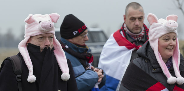 Pegida-Anhänger_innen tragen Schweinchen-Mützen auf dem Kopf