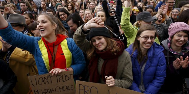 Viele junge Frauen, die vorderste Reihe hält Plakate in den Händen, eine Frau hält einen Kleiderbügel