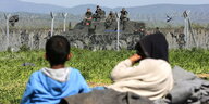 Flüchtlinge liegen vor dem Grenzzaun in Idomeni, dahinter mazedonische Polizisten