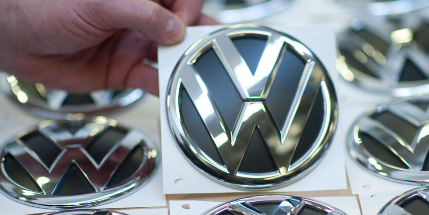 Eine Hand hält ein silbernes VW-Symbol