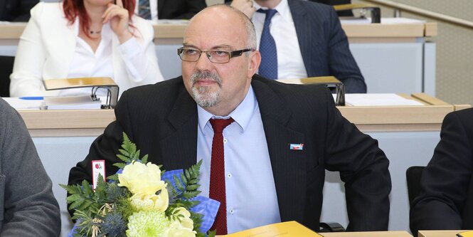 Ein Mann sitzt im Landtag von Sachsen-Anhalt. Vor ihm stehen Blumen auf dem Tisch