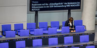 Eine Saalhelferin sitzt im Bundestag, im Hintergrund ein Schild mit der Themenankündigung