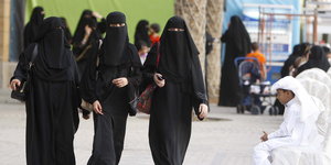 Drei verschleierte Frauen laufen über einen Platz
