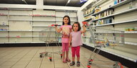 Zwei kleine Mädchen stehen mit Einkaufswagen vor fast leeren Regalen bei Schlecker